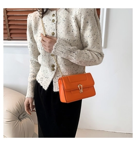 Détail d'un petit sac bandoulière orange vif avec fermoir en U doré et chaîne dorée