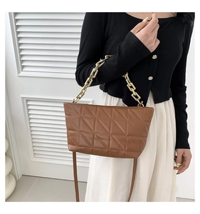 Detail of a brown quilted leather crossbody bag with a gold chain and a slim leather strap