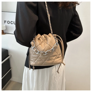 Detail of beige quilted bucket bag with silver chain handle worn by a model in a blazer