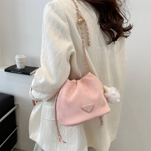 Pink drawstring bucket bag with golden chain and plush ball worn by a model