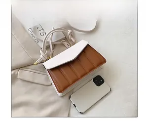 Detailed comparison of color-block handbag size with a smartphone on a beige fabric