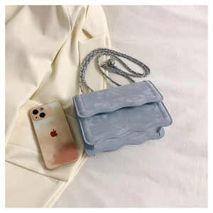 Close-up of light blue crossbody bag with wave edges and silver chain on white fabric