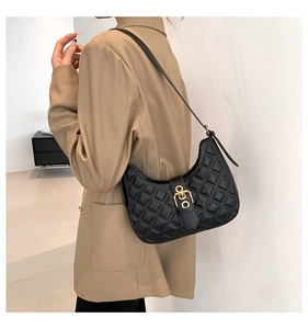 Détail d'un sac à bandoulière matelassé noir avec boucle dorée sur un blazer kaki