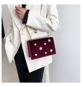 Détail d'un sac chaîne en velours violet foncé avec clous dorés porté par un modèle