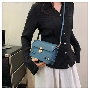 Close-up of misty blue crossbody bag with gold round clasp and leather buckle details
