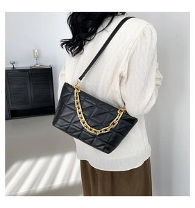 Quilted black crossbody bag with gold chain strap shown on model in a minimalist setting