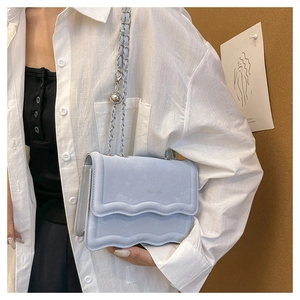 Close-up of light blue crossbody bag featuring a wavy flap design and silver chain strap