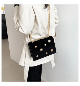 Détail d'un sac bandoulière en velours noir avec bijoux dorés sur un manteau blanc chic