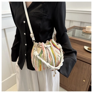 Detail of colorful striped woven bucket bag featuring elegant white leather handle and straps