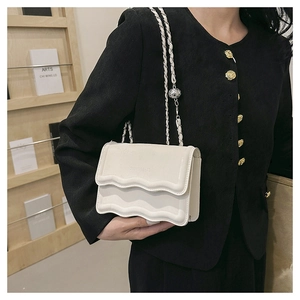 Chic white crossbody flap bag with wave edge design and chain strap on a model