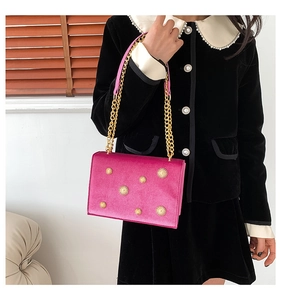 Détail du sac bandoulière en velours rose avec breloques dorées en forme de soleil et chaîne