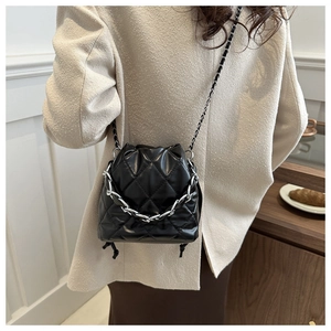Detail of black quilted leather bucket bag with silver chain strap on model in cafe