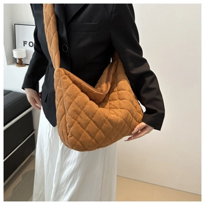 Detailed view of brown corduroy quilted tote bag shown on a person's shoulder