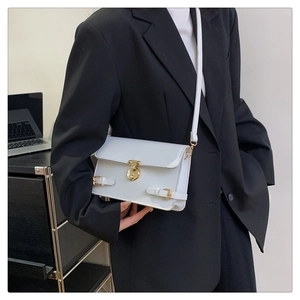 Close-up of stylish white crossbody bag with golden round buckle and leather texture