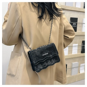 Detailed view of black wavy flap crossbody bag with silver chain strap on model