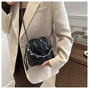 Detail of black quilted bucket bag featuring metallic chain handles and glossy leather texture