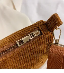 Detail of a brown corduroy bag with shiny gold metal zipper and textured wide shoulder strap