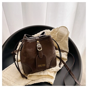 Detail of a dark brown bucket bag with drawstring closure and metal buckle on soft fabric