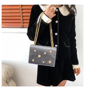 Détail d'un sac bandoulière en velours gris avec rivets soleil dorés et bandoulière chaîne