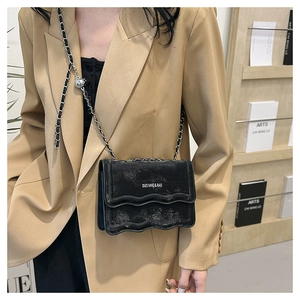 Detail of wave pattern black crossbody bag with silver chain strap and metal buckle