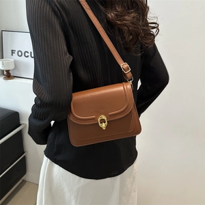 Brown leather crossbody square bag with gold metal clasp shown on a model's shoulder
