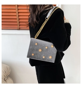 Détail du sac bandoulière en velours gris avec clous floraux dorés et chaîne élégante