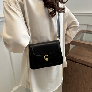 Minimalist black crossbody flap bag with gold rings shown on a stylish model