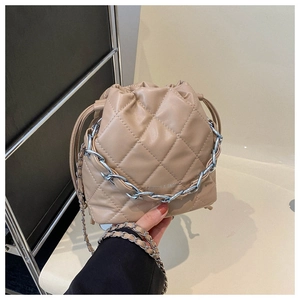 Detailed macro view of quilted beige bucket bag featuring silver chain handle and drawstring