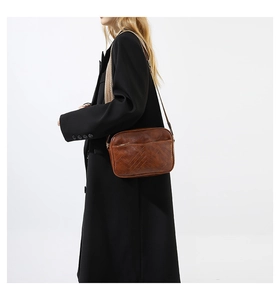 Brown leather crossbody bag detail featuring V-shaped stitching and patterned strap