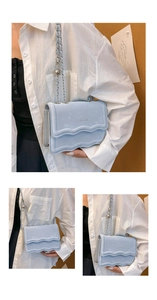 Detail of light blue crossbody bag with wavy pleats and silver chain strap with ball charm