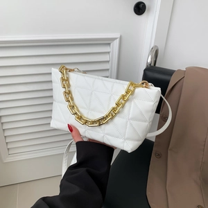 Quilted white crossbody bag with gold chain strap displayed on a chair with a brown blazer