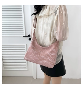 Pale pink glossy pleated underarm bag worn by a model in a minimalist setting