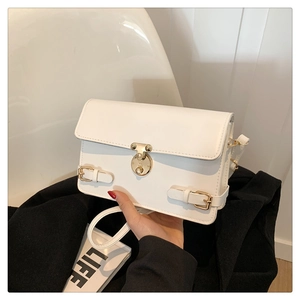 Detail view of white faux leather square bag with gold twist lock and flap closure
