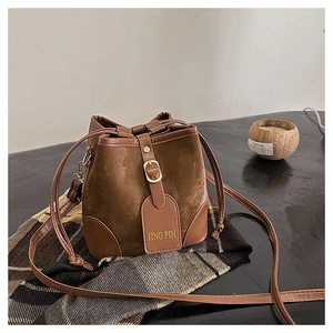 Close-up of a brown suede drawstring bucket bag with gold hardware and leather details