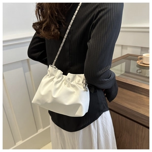 Detail view of cream pleated bucket bag with silver chain strap worn by a model