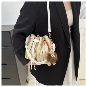 Close-up of knitted bucket bag with vertical stripes and a cute brown plush monster charm