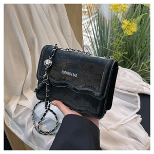 Detail of black crossbody bag with textured leather, chain strap, and sphere pendant