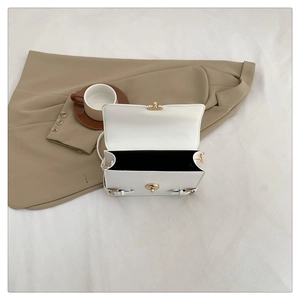 Detail of white leather crossbody bag featuring gold twist lock and black fabric lining