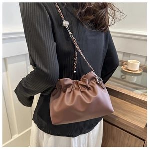 Detail view of brown pleated cloud bag with silver chain strap and spherical charm