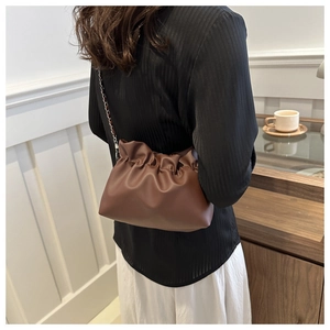 Detail view of the brown pleated cloud bucket bag worn with a delicate metal chain strap