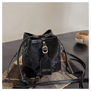 Detail of black pebbled leather bucket bag with gold buckle and drawstring closure