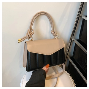 Detail of beige and black patchwork handbag with vertical quilting and knotted handle
