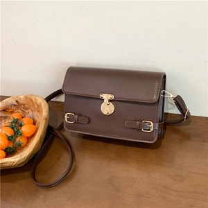 Vintage dark brown leather crossbody bag with golden rotary lock on a rustic wooden desk