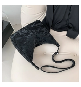 Detail of black pleated nylon tote bag featuring adjustable strap on white background