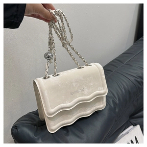 Detail of cream crossbody bag featuring wavy edges and elegant silver chain strap