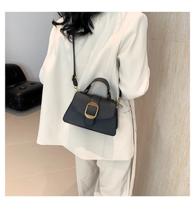 Détail d'un sac à main en cuir noir avec une boucle carrée dorée texturée très apparente