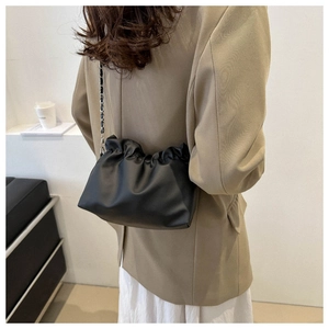 Detail view of black pleated bucket bag with metal chain strap worn by a model