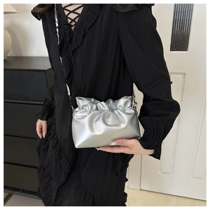 Detail of silver pleated bucket bag with chain strap worn with a black dress