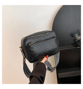 Close-up of black crossbody bag with geometric quilting and wide woven shoulder strap