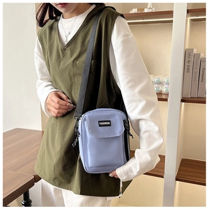 Detail of light blue nylon crossbody bag with Fashion label worn over olive vest